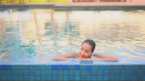 Beautiful-Asian-woman-approach-the-swimming-pool-border-and-lean-on-the-edge-smiling,-tropical-Hotel-vacation