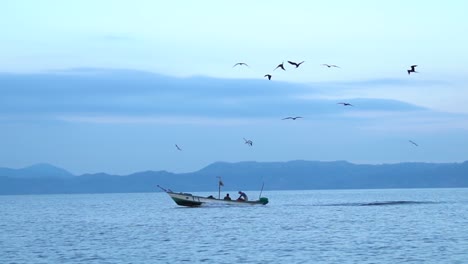 Slow-motion-shot:-a-fisherman-driving-a-boat-at-sea,-surrounded-and-followed-by-hungry-seagulls
