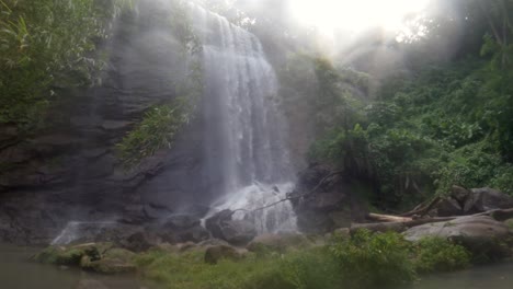 A-waterfall-in-the-jungle-with-a-heavy-mist-blowing-in-the-wind-and-the-sun-shining-in-the-sky