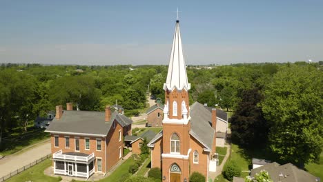Aerial-Establishing-Shot-of-Traditional-White-Steeple-Church-behind-Green-Trees-in-Summer