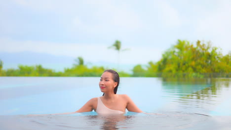 Mujer-Sexy-En-Forma-Relajándose-Dentro-De-La-Piscina-Al-Aire-Libre,-Exótico-Hotel-Spa-Con-Traje-De-Baño-De-Un-Solo-Hombro-Sobre-Un-Exuberante-Fondo-Verde-En-Bali