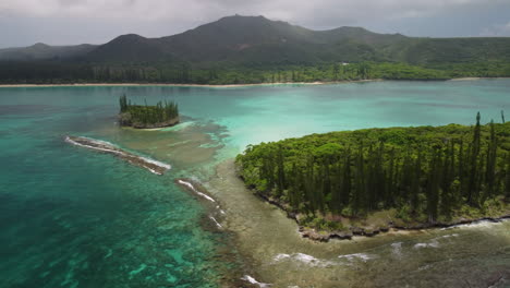 Aerial-arc-above-turquoise-water-and-small-islands,-N'ga-peak-in-background,-Isle-of-pines