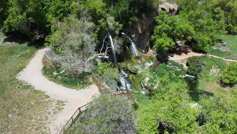 Aerial-view,-female-at-lookout-above-Rifle-Falls-on-sunny-summer-day,-waterfalls-and-green-landscape-of-Colorado-State-Park,-drone-shot