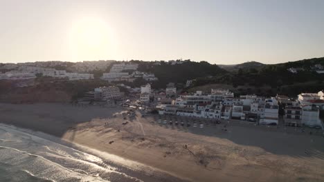 Aerial-of-Salema-beach-depicting-its-promenade,-resorts-and-beach-umbrellas-during-sunset