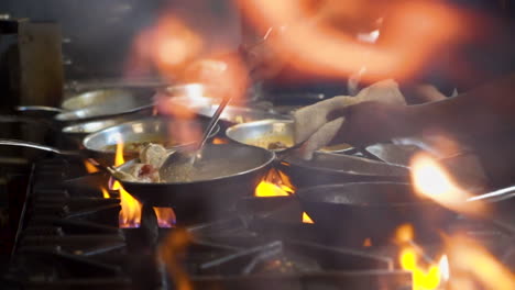 Chef-sautes-dishes-over-flames-in-restaurant-kitchen,-Foreground-flare-up-from-stove,-cinematic-slider-slow-motion-HD