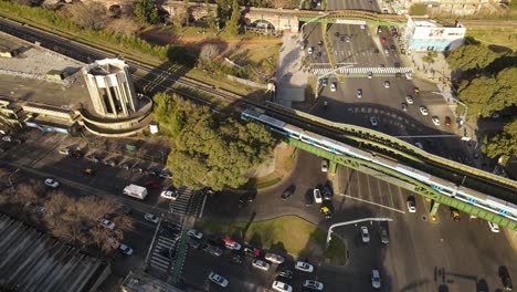 Aerial-top-down-shot-of-traffic-on-road-and-driving-train-over-bridge-during-rush-hour-in-Buenos-Aires
