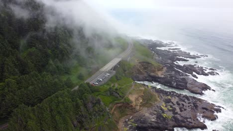 4K-30FPS-Aerial-Footage-Oregon-Coast---Epic-Tracking-Shot-of-US-Route-101-and-car-traffic--Flying-amongst-clouds,-waves-crashing-against-mossy-stone-rocky-Pacific-Ocean-Shore---DJI-Drone-Video