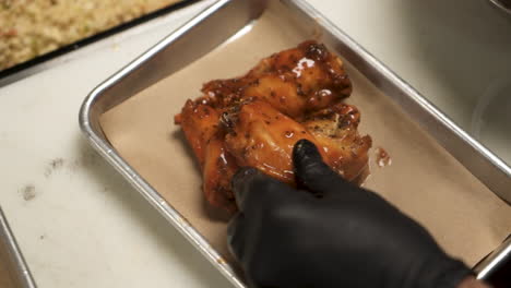 Chef-neatly-stacks-freshly-sauced-buffalo-chicken-wings-on-metal-tray,-slow-motion-4K