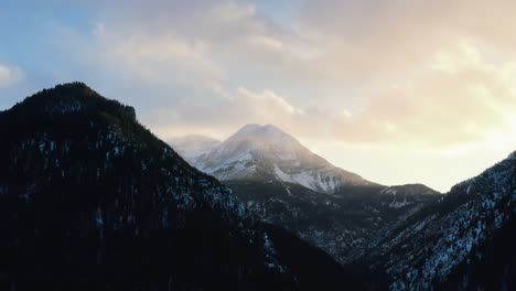 Aerial-drone-Time-lapse-of-a-winter-landscape-of-Mount-Timpanogos-in-the-background-surrounded-by-a-pine-tree-forest-during-sunset-from-the-frozen-Tibble-Fork-Reservoir-in-American-Fork-Canyon,-Utah