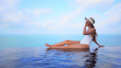 An-attractive-young-woman-appears-to-be-floating-in-midair-along-the-water's-edge-of-an-infinity-edge-pool,-ocean-background