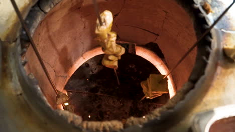 Long-skewer-of-tandoori-chicken-is-removed-from-traditional-tandoor-oven-in-Indian-kitchen,-slider-close-up-slow-motion-HD