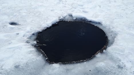 A-small-hole-with-bubbles-rising-to-the-surface-in-the-frozen-Tibble-Fork-reservoir-lake-for-ice-fishing-in-American-Fork-Canyon,-UT