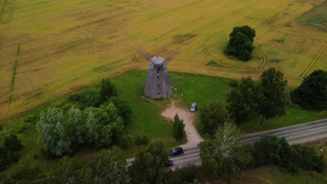 aerial-shot-of-an-old-windmill-in-the-field-by-the-road,-zooming-out