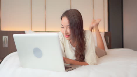 Close-up-woman-lying-prone-on-a-bed-works-on-her-laptop
