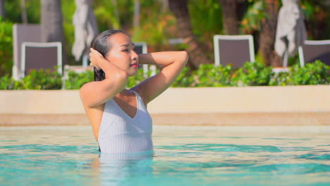 Eine-Leidenschaftliche-Junge-Asiatin-Berührt-Ihr-Nasses-Haar-Im-Poolwasser-Eines-Exotischen-Hotels-Mit-Geschlossenen-Augen-Bei-Sonnenuntergang-Im-Miami-Hotel,-Porträtaufnahme