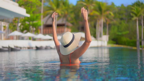 A-woman-with-her-back-to-the-camera-holds-on-to-the-edges-of-her-sun-hat-as-she-reacts-to-the-joy-of-being-on-vacation