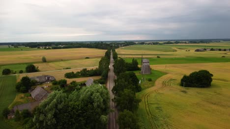 aerial-shot-of-an-old-windmill-in-the-field-by-the-road,-drone-shot