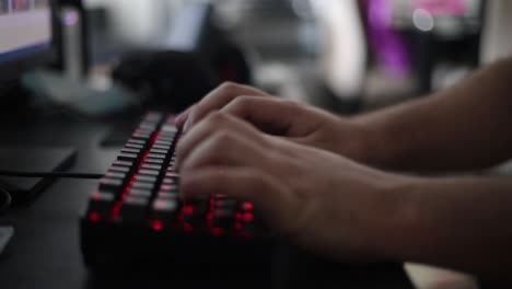 medium-static-shot-of-a-young-man-using-a-mechanical-keyboard-with-red-leg-lighting-next-to-a-led-lighting-mouse-with-blurred-household-elements