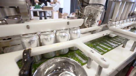 Industrial-canning-machine-tops-and-seals-cans,-four-aluminum-beverage-cans-move-down-production-line,-HD