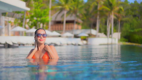 Slowmo---woman-inside-tropical-swimming-pool-touching-her-were-hair-and-walking-sensually-looking-at-camera-lense,-Bora-Bora-hotel