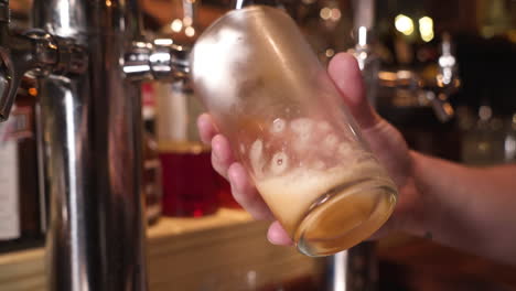 Bartender-pulls-draft-amber-beer-into-frosted-pint-glass,-tracking-close-up-HD