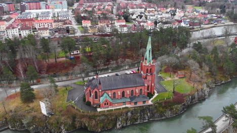 Dolly-out-aerial-view-of-distinctive-neo-Gothic-style-Trollhättan-church-located-on-cliff-in-Göta-river,-Västra-Götaland-County-Sweden