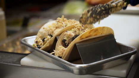 Chef-tops-fish-black-bean-tacos-with-slaw,-cook-plates-tacos-in-taco-stand-rack-with-coleslaw,-slow-motion-close-up-4K