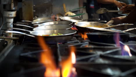 Professional-restaurant-kitchen-staff-stir-saute-various-dishes-over-high-heat-range-top-stove-with-flare-ups,-cinematic-slow-motion-slider-HD