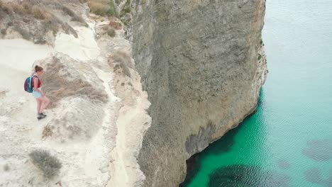 Female-Hiker-on-Top-of-Steep-Cliff-Above-Mediterranean-Sea,-Coastline-of-Malta,-Scenic-Landscape-on-Summer-Day,-Wide-View