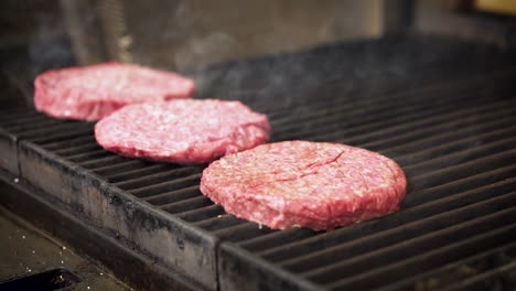 Cook-seasons-sizzling-hamburger-patties-as-smoke-rises-from-grill,-4K