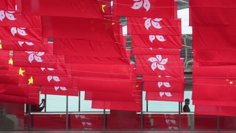 Pendler-Gehen-Durch-Eine-Fußgängerbrücke,-Während-Die-Flaggen-Der-Volksrepublik-China-Und-Der-Hongkong-Sar-In-Einer-Straße-Während-Des-Jahrestags-Der-übergabe-Hongkongs-An-China-Zu-Sehen-Sind