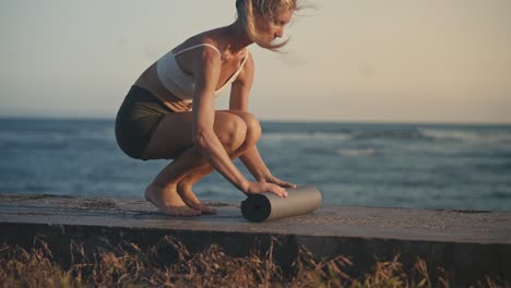 Una foto horizontal de una mujer delgada motivada vestida con ropa  deportiva se prepara para poses de entrenamiento duro con una colchoneta de  fitness enfocada en poses a distancia contra una pared