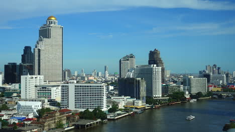 Time-Lapse-of-the-river-traffic-in-front-of-the-State-Tower-building-and-its-golden-dome-downtown-Bangkok,-Thailand