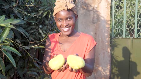 An-African-woman-holding-up-two-freshly-picked-mangoes-and-smiling-at-the-camera