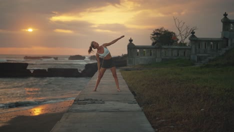 Woman-doing-yoga-on-Bali-shore-at-sunset-performing-Triangla-Pose,-asana