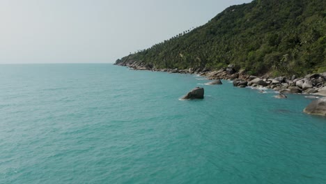 Tropical-shore-of-Koh-Phangan-with-large-boulders,-calm-blue-water