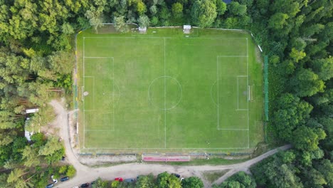 Ascending-aerial-top-down-shot-of-empty-football-soccer-field-surrounded-by-green-forest-trees-in-suburb