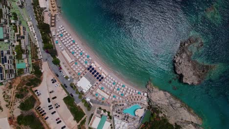 Vacation-resort-and-beach-umbrellas-near-blue-turquoise-sea-water-in-Mediterranean,-top-down-view