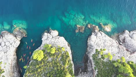 Vista-Aérea-Ascendente-De-Un-Grupo-De-Turistas-En-Kayaks-Pasando-Por-La-Isla-De-Lokrum-Cerca-De-Dubrovnik-En-La-Costa-Adriática-De-Croacia