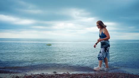 Senior-Woman-Walking-At-The-Beach-In-Karkle,-Lithuania---wide,-slow-motion