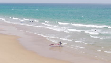 Una-Persona-Tomando-Su-Vela-Y-Preparándose-Para-Practicar-Windsurf-En-La-Praia-Do-Guincho,-Portugal