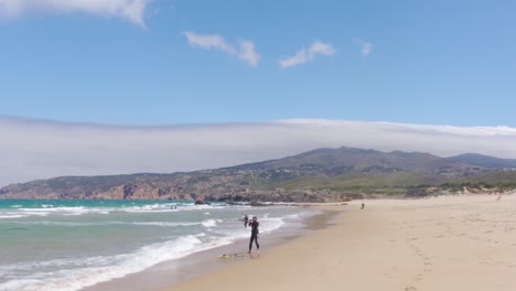 Un-Windsurfista-Ajustando-Su-Vela-Y-Preparándose-Para-Entrar-Al-Agua-En-Praia-Do-Guincho,-Portugal