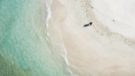 Aerial---Single-woman-tourist-wearing-sarong-strolls-on-beach-during-summer-vacation,-near-Puerto-Plata