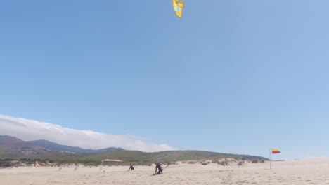 Un-Windsurfista-Ajustando-Su-Vela-Y-Caminando-Hacia-El-Agua-En-Praia-Do-Guincho,-Portugal