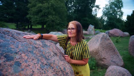 A-Senior-Woman-Enjoying-Walking-Around-With-Hands-Touching-On-Big-Rock-Boulders-At-The-Park-Near-Karkle,-Lithuania