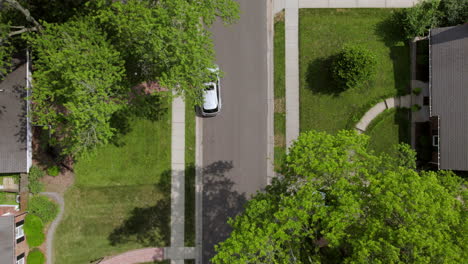 Overhead-of-a-white-car-pulling-out-of-a-driveway-in-a-suburban-neighborhood-and-then-driving-away-as-camera-rises