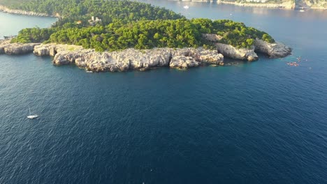 Aerial-view-of-a-group-of-tourists-on-a-kayak-tour-and-boat-passing-by-Lokrum-Island-near-Dubrovnik-on-the-Adriatic-coastline-of-Croatia