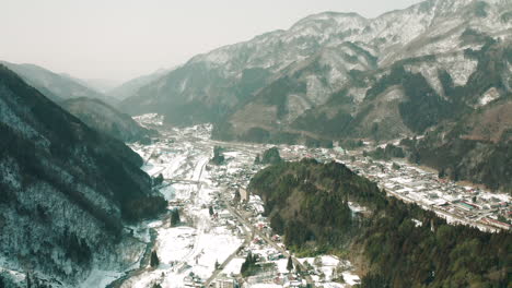 Panoramic-View-Of-A-City-In-Deep-Snow-With-Towering-Forest-Mountains-In-Okuhida-Hirayu,-Gifu,-Japan