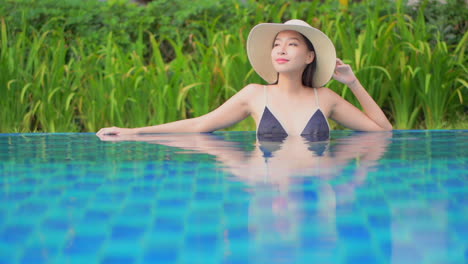 Sexy-asian-woman-in-colorful-tropical-scenery-blue-swimming-pool-water-and-green-vegetation,-full-frame,-slow-motion