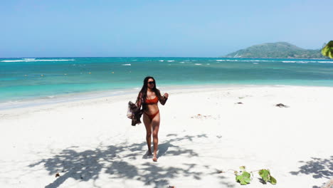 Hispanic-woman-enjoys-leisure-getaway-to-secluded-white-sand-beach-paradise-in-Caribbean,-drone-dolly-out